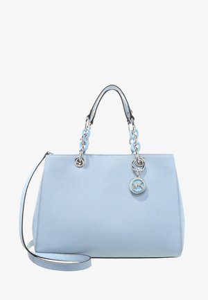 Sac à main en cuir bleu clair avec deux poignées ornées de maillons de chaîne argentés et bleus, une bandoulière amovible et un pendentif rond en argent avec le logo MK.