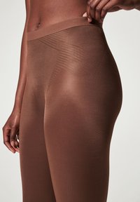 Brown leggings with a smooth, stretchy texture. Features a wide waistband and subtle vertical pattern along the side, highlighting the fit.