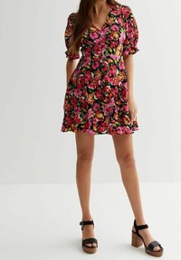 Robe florale avec un fond noir, ornée de fleurs roses, orange et vertes, avec des manches bouffantes courtes, un décolleté en V et une jupe évasée.