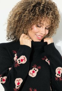 Schwarzer Pullover mit hohem Kragen, der ein Rentiermuster in Pink und Rot zeigt. Weicher Stoff, enganliegende Ärmel und detailliertes Strickdesign.