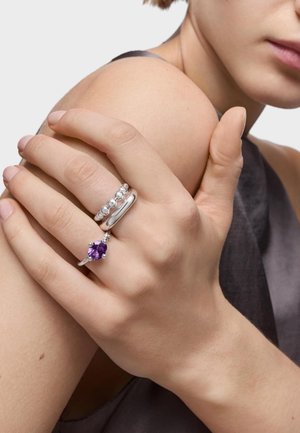 Three metallic rings on a hand: one silver band, one with silver beads, and one with a purple gemstone set in silver.