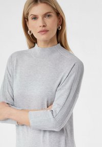 Hellgrauer Pullover mit hohem Kragen, gerippten kurzen Ärmeln und weicher Textur, entworfen für eine lässige Passform.