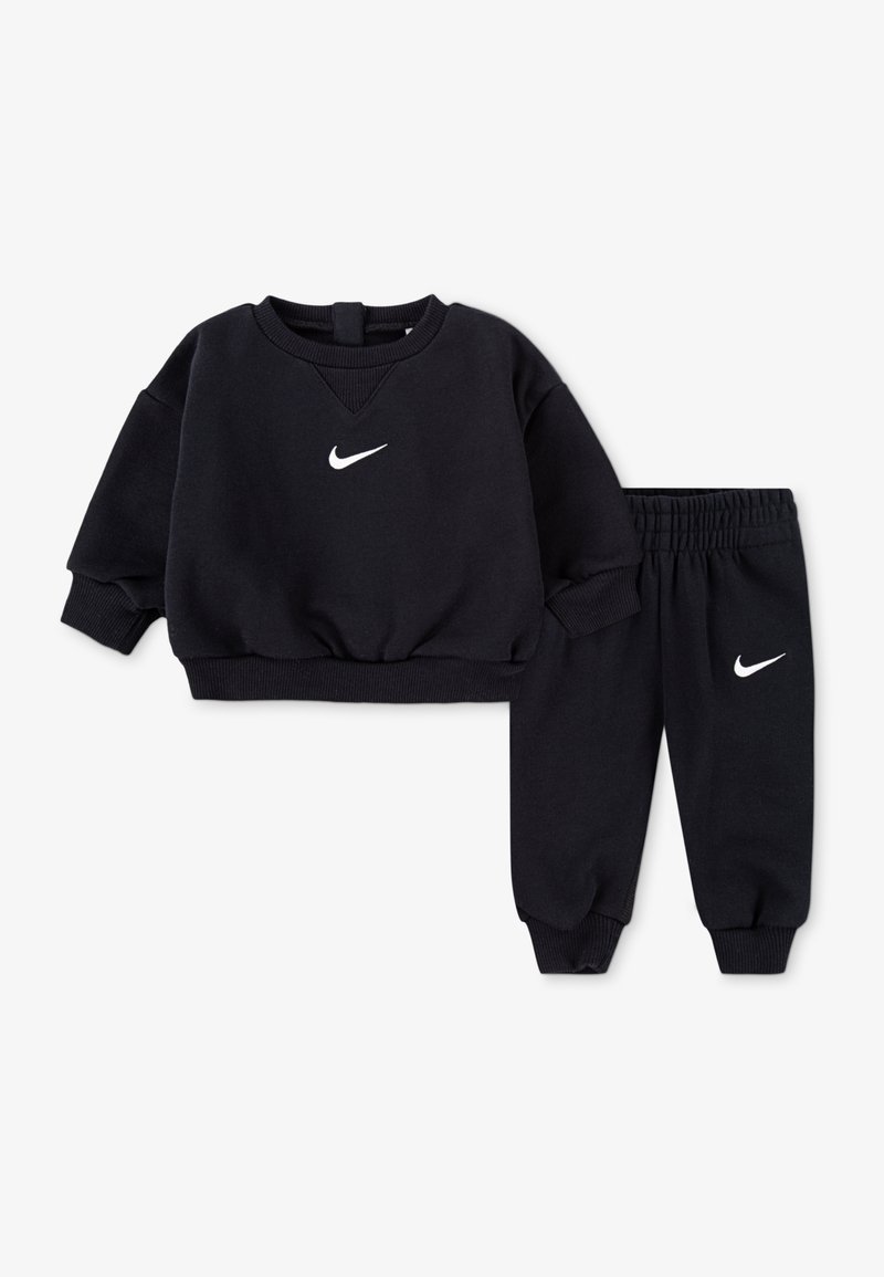 Czarna bluza polarowa z długimi rękawami i okrągłym dekoltem, z białym logo Nike. Dopasowane czarne spodnie dresowe z elastycznym pasem i ściągaczami przy nogawkach.