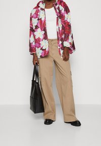 Floral print, hooded windbreaker in pink and purple; white tank top; beige cargo pants with pockets; black tote bag; black footwear.