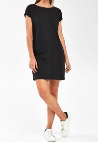 Robe courte noire à manches courtes avec un col rond, confectionnée dans un tissu lisse et léger. Associée à des baskets blanches et noires.
