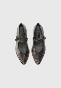 Pekete flats med spiss tå i brunt og svart slangeskinn. Har en smal stropp med en rund spenne. Glatt innermateriale.