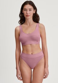 Soutien-gorge de sport rose clair avec une large bande et un col arrondi, associé à une culotte taille haute assortie, toutes deux en tissu lisse et extensible.