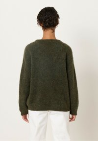 Žalias vilnonis megztinis, atsipalaidavusio silueto, apvaliu kaklu ir ilgomis rankovėmis. Audinys minkštas ir pūkuotas, su šiek tiek per dideliu siluetu.