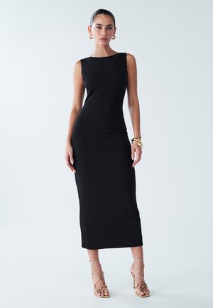 Black sleeveless dress, fitted design, knee-length, smooth fabric. Paired with strappy gold high-heeled sandals and minimalist jewelry.