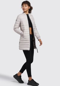 Geacă puffer gri deschis cu cusături orizontale, guler înalt și buzunare laterale. Asortată cu blugi skinny negri și adidași.