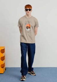 Lichtbeige NASA graphic t-shirt met ronde hals, gecombineerd met donkerblauwe rechte jeans en meerkleurige sneakers. Zwarte zonnebril gedragen.