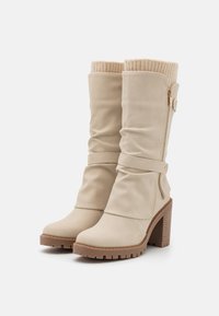 Botas altas de rodilla de imitación de piel beige con un diseño arrugado, parte superior de punto acanalado y cremallera lateral, con un tacón grueso y suela texturizada.