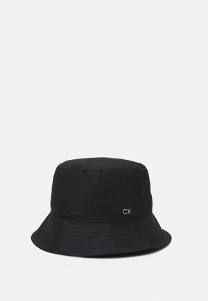 Czarny kapelusz typu bucket z perforowanym wzorem logo "CK" oraz małym, białym haftowanym napisem "CK" po boku, pokazany na jednolitym jasnym tle.