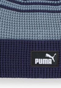 Gebreide beanie in grijs en marineblauw met ribbeltextuur. Heeft een zwart Puma logo sticker aan de onderkant. Klassieke ronde vorm.