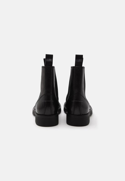 Paire de bottines en cuir noir vues de dos, avec tirants et petits talons, sur fond blanc.