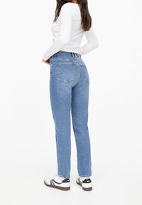 Höga blå denimjeans med rak passform, två bakfickor och en blekt finish, tillsammans med en vit långärmad topp och sneakers.