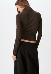 Brun långärmad topp med krage, figurnära design och ribbad textur, kombinerad med svarta byxor med elastisk midja och lös passform.
