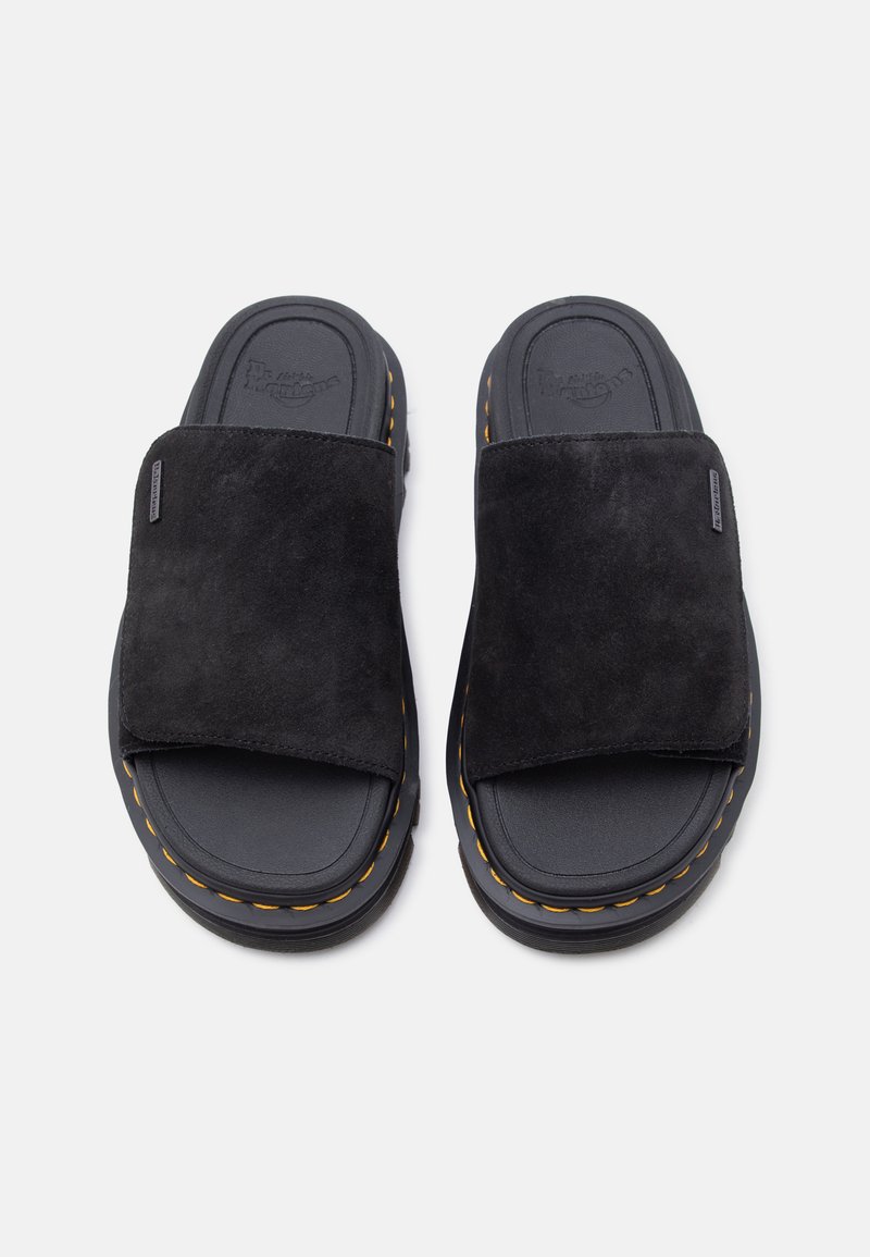 Sandali slip-on in suede nero con suole spesse, cuciture gialle lungo i bordi e etichette con marchio sulle fasce larghe.