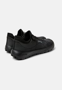 Schwarze Sneakers aus strukturiertem Stoff mit einer gepolsterten Sohle, die ein abgerundetes Design und minimale Markenkennzeichnung an der Seite aufweisen.