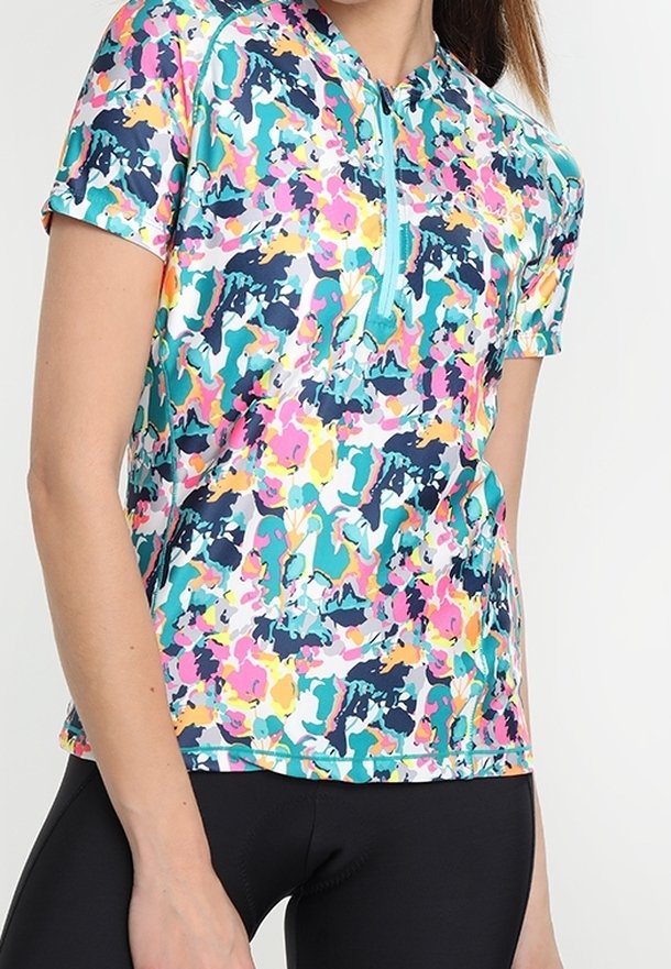 Mujer con un top deportivo de manga corta, colorido con flores y cremallera, y pantalones cortos de ciclismo ajustados negros, torso visible sobre un fondo liso.