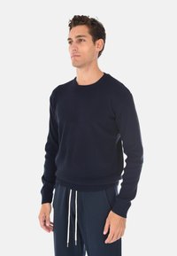 Maglione a coste blu navy con collo tondo e maniche lunghe, abbinato a pantaloni della tuta blu scuro con cordoncino.
