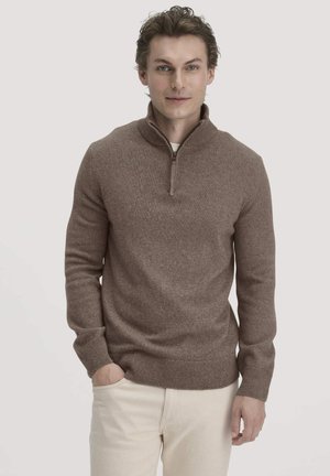 Bruine pullover sweater met een kwart-rits kraag, textuur gebreid materiaal, ribgebreide manchetten en zoom, gedragen over een licht shirt, gecombineerd met lichte broeken.