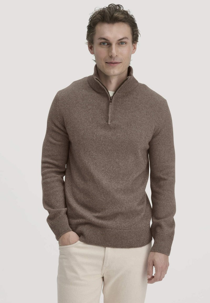 Brauner Pullover mit einem Viertel-Reißverschluss-Kragen, aus strukturiertem Strickmaterial, mit gerippten Bündchen und Saum, getragen über einem hellen Hemd, kombiniert mit hellen Hosen.