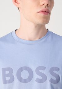 T-shirt en coton bleu clair avec un grand logo gris "BOSS" en évidence au centre. Encolure ronde et manches courtes. Texture lisse.