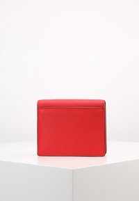 Borsa a mano rossa in pelle con una texture liscia, forma rettangolare e chiusura superiore piatta. Design minimalista con dettagli di cuciture a contrasto.