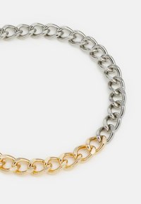 Colar de corrente de metal misto com elos alternados em prata e ouro, cada um com um acabamento polido e design entrelaçado.