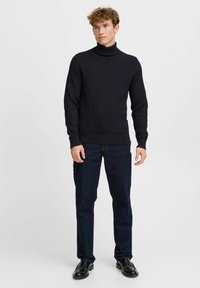 Maglione lavorato a maglia blu navy con un motivo a trama, colletto alto e polsini a coste, abbinato a jeans scuri e scarpe nere.