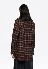 Camisa de cuadros negra y naranja de manga larga con un corte relajado, puños con botones y dobladillo curved. Tejido suave con una apariencia ligeramente texturizada.