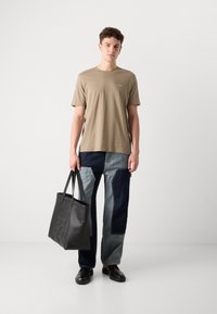 Beige bomulds t-shirt med grønt logo, parret med patchwork denim bukser i forskellige nuancer af blå. Sort læder tote taske med præget detalje.
