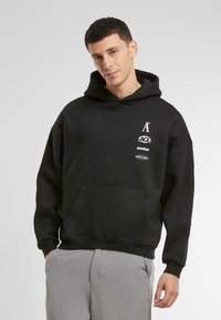 Zwarte hoodie met een voorzak, voorzien van witte bedrukte logo's. Zachte katoenmix met ribgebreide manchetten en zoom.