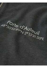 Tissu en charbon de bois avec texte blanc indiquant "Porte d'Auteuil" et les coordonnées géographiques 48°50'52.89"N 2°15'31.50"E, à côté d'une fermeture éclair.