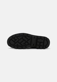 Suela de zapato de goma negra con un patrón de agarre texturizado que presenta profundas ranuras y áreas elevadas para tracción. Etiqueta incrustada en el lateral.