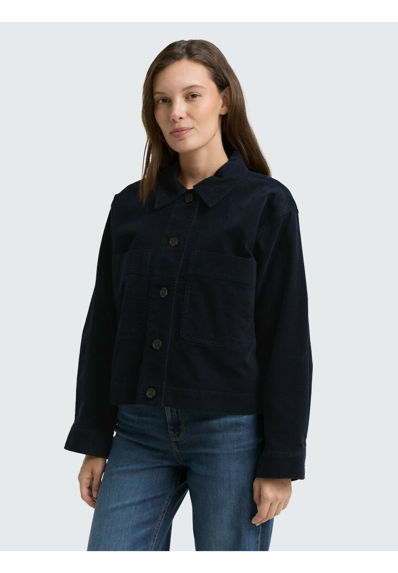 Donkerblauwe corduroy jas met een kraag, sluiting met knopen aan de voorkant en twee grote opgestikte zakken. Ontworpen met lange mouwen en een relaxte pasvorm.