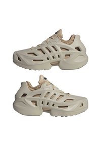 Beige urheilujalkineet, joissa on hengittävä verkkopinta, aaltoilevat linjat ja useita viiltoja ilmanvaihtoa varten. Teksturoitu yksityiskohta kaulassa.