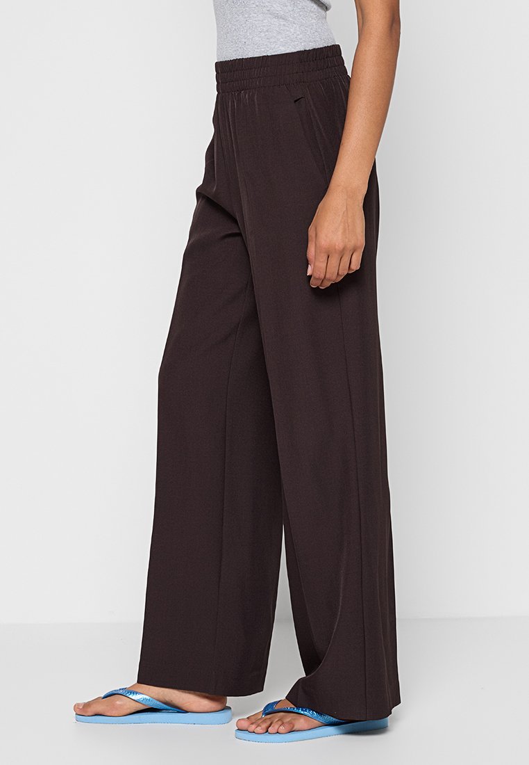 Bruine wijde broek met een elastische tailleband, gemaakt van een zachte stof. Gecombineerd met blauwe slippers, met een platte zool en een eenvoudig ontwerp.