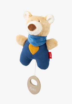 Weicher Plüschbär mit beigem Fell, blauer Schleife und blauen Hosen mit einem gelben Herz. Enthält einen Zugfaden und einen runden Ring.