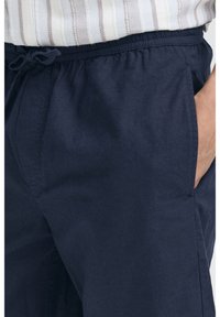 Marineblå letvægtsbukser med elastik i taljen, snøre-detalje og sidelommer. Stoffet virker glat og mat.