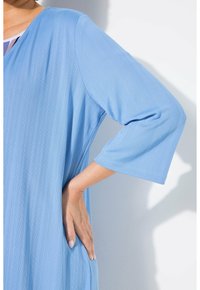 Hellblaue Tunika mit vertikaler Rippstruktur, V-Ausschnitt und Dreiviertelärmeln, mit lockerem Schnitt und seitlichen Schlitzen.