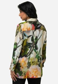 Bluse mit Floralprint in lebhaften Farben und glänzender Textur. Die Rückansicht zeigt mehrfarbige Rosen und Blätter, mit langen Ärmeln und Manschettenakzenten.