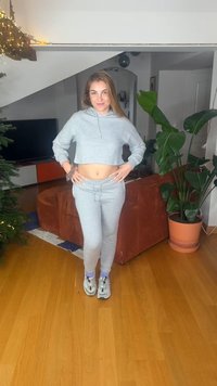 Ανοιχτό γκρι cropped φούτερ και ταιριαστά παντελόνια τζόγκινγκ. Μαλακή υφή, ελαστική μέση, φορεμένα με λευκά αθλητικά παπούτσια και μωβ κάλτσες. Εσωτερικός χώρος.