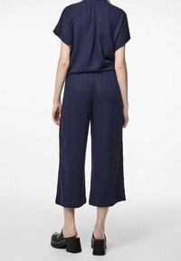 Completo in lino blu navy con maniche corte e elastico in vita, caratterizzato da pantaloni larghi e cropped. Mule con tacco a blocco neri completano l'outfit.