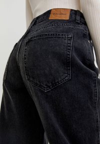 Vaqueros de mezclilla negra con una cintura alta, que presentan un parche de cuero etiquetado "PULL&BEAR" y un diseño tradicional de bolsillo trasero.