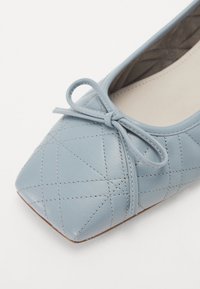 Ballet flat en cuir bleu clair avec un bout carré, un motif matelassé et un accent en forme de nœud à l'avant. L'intérieur présente une doublure beige.