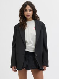 Svart blazer med en strukturerad design, som har två framskjutna knappar och en skräddarsydd passform. Bärs över en ljusgrå sweatshirt och lager-på-lager med en svart kjol.