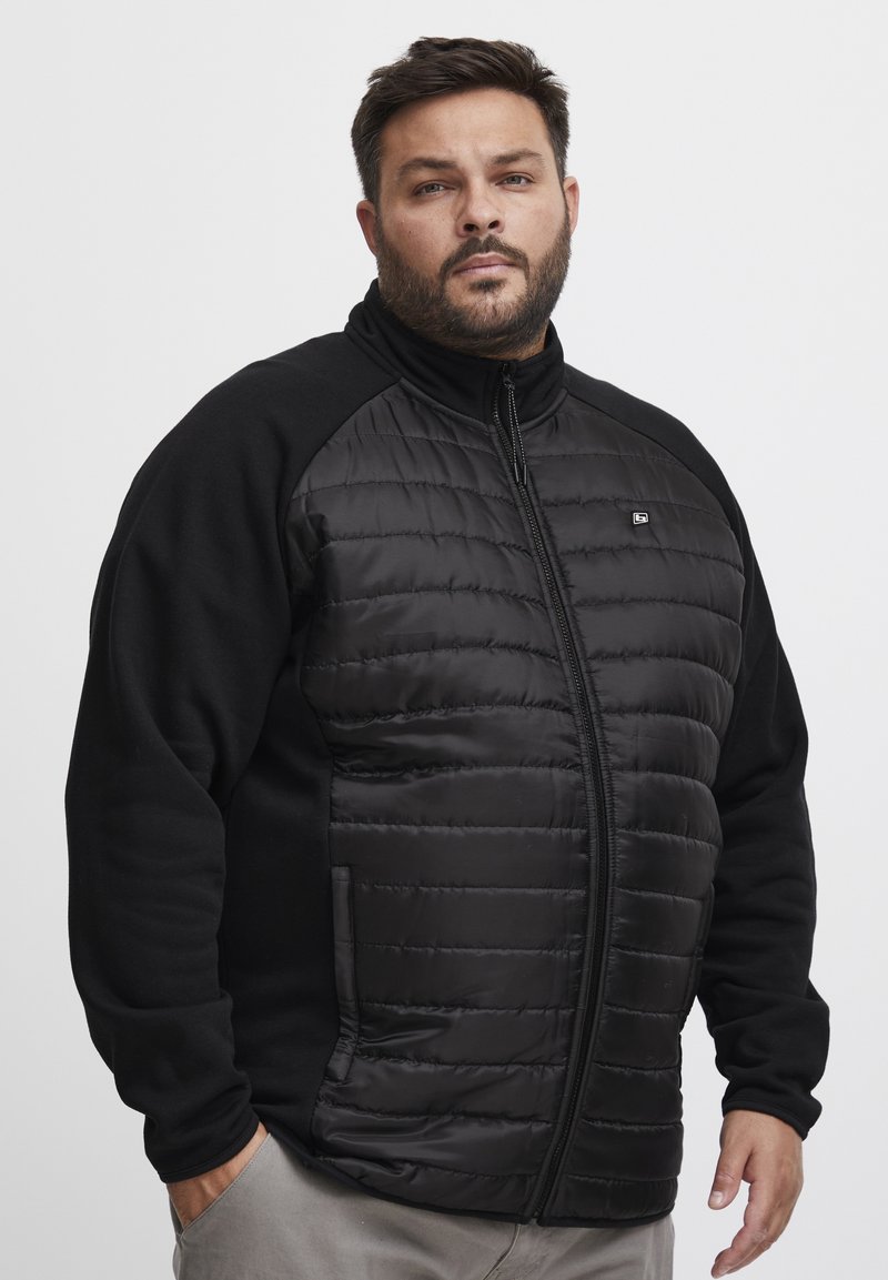 Black puffer jacket with a solid black fleece torso and sleeves. Features a full zipper, stand collar, and side pockets. Textured fabric on front.