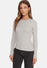 Maglietta grigia a maniche lunghe in materiale morbido, con design aderente e scollo rotondo, con un marchio discreto al centro.